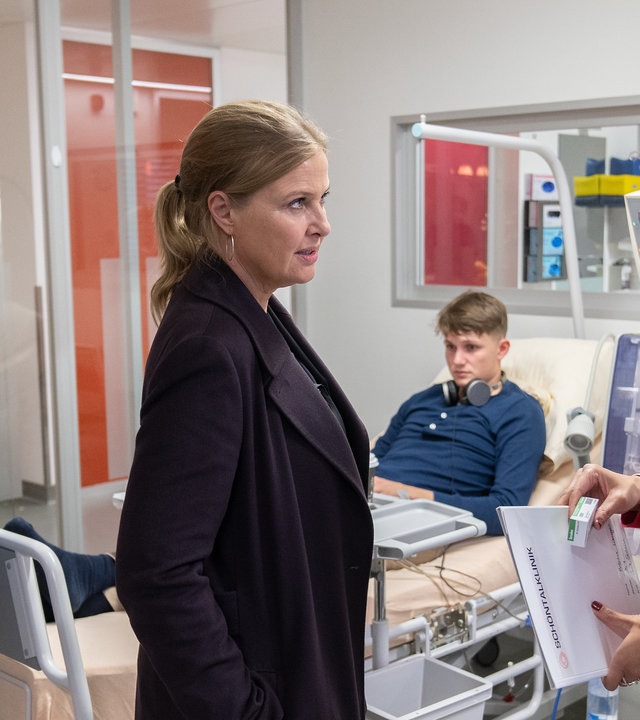 "Die Chefin - Deadline": Das Gespräch im Krankenhaus. Vera Lanz (Katharina Böhm) und Korbinian Kirchner (Jonathan Hutter) stehen der Ärztin Dr. Leyla Sahin (Pegah Ferydoni) gegenüber, sie sind alle von der Seite zu sehen. Im Hintergrund ist das Krankenbett mit dem Patienten Florian Blanke (Leon Blaschke) zu sehen.
