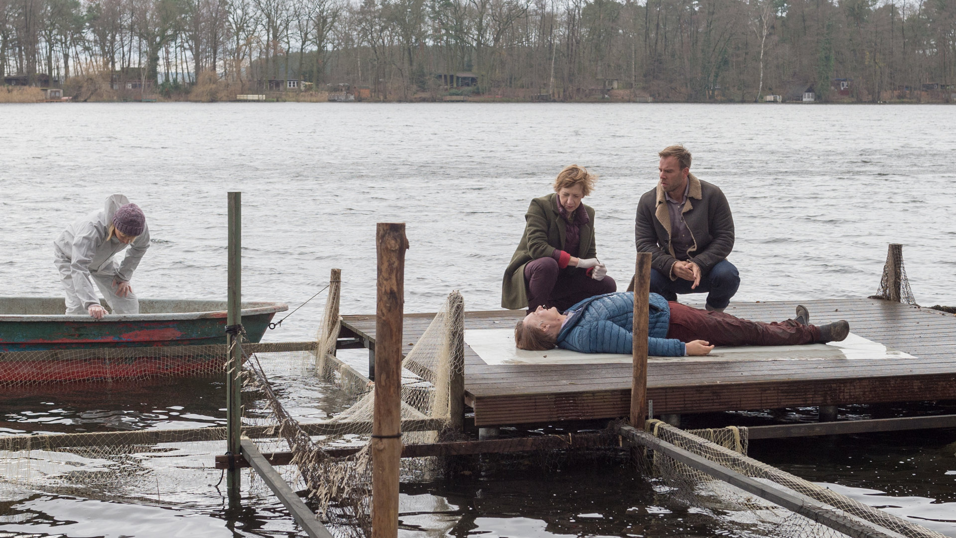 „SOKO Wismar – Kalt serviert“: Auf einem Steg am See liegt die Leiche von Arne Bahlbeck (Klaus Christian Schreiber). Neben ihm knien Helene Sturbeck (Katharina Blaschke) und Lars Pöhlmann (Dominic Boeer). Roswitha Prinzler (Silke Matthias) von der Kriminaltechnik untersucht derweil ein Boot, das auf dem See treibt.