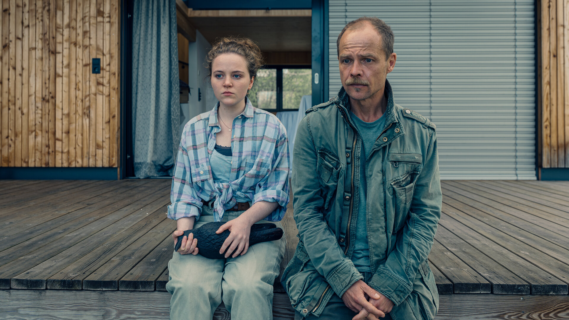 "Die Toten vom Bodensee - Das Geisterschiff": Lenka Bergdorf (Alice Prosser) und Micha Oberländer (Matthias Koeberlin) sitzen nebeneinander auf einem Bootssteg. Lenka Bergdorf hält eine Figur in der Hand.