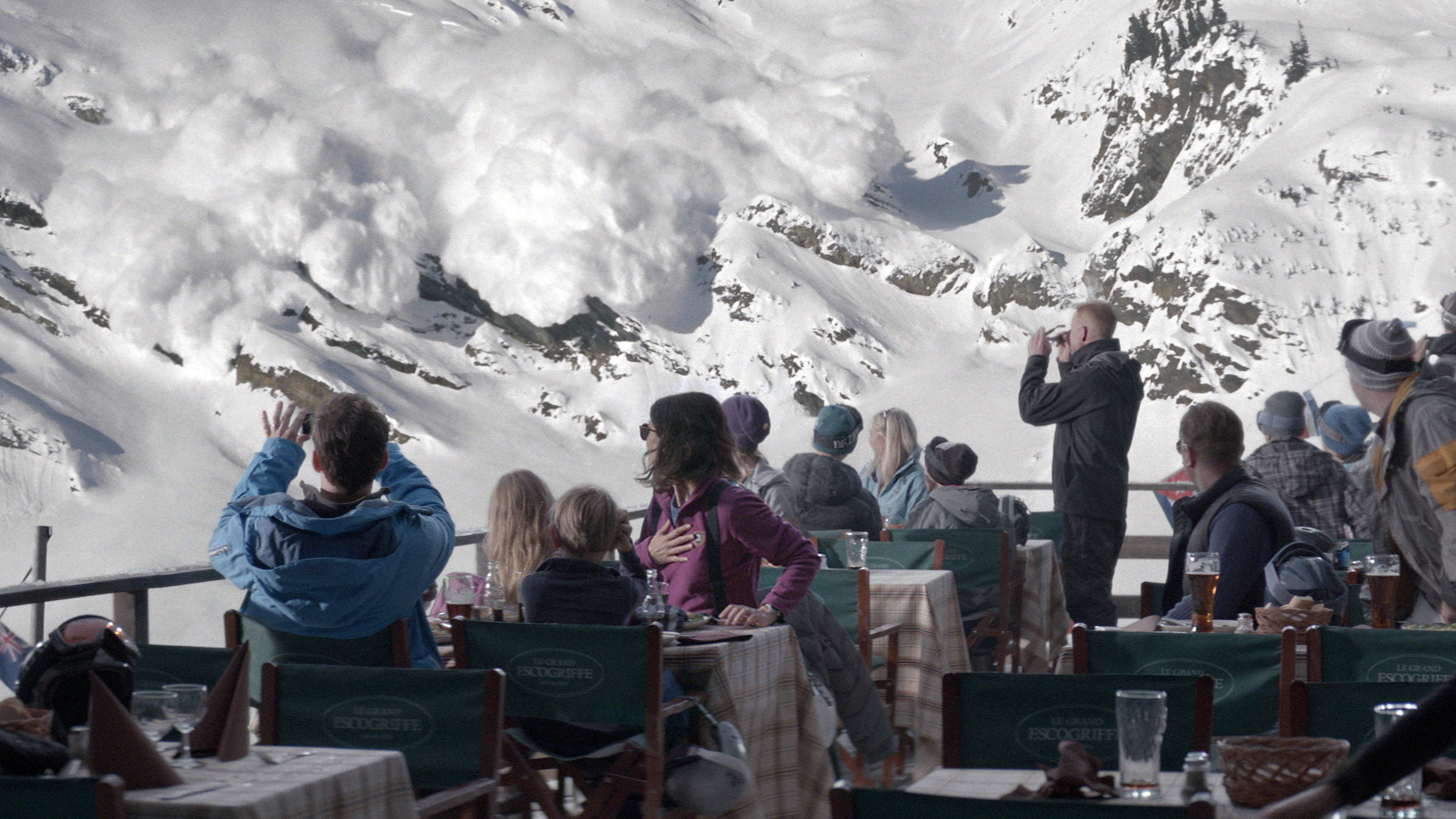 "Höhere Gewalt": Auf der Terrasse einer bewirtschafteten Berghütte sitzen viele Skifahrer. Sie beobachten verwundert und auch erschrocken den Abgang einer Lawine, die man im Hintergrund sieht.