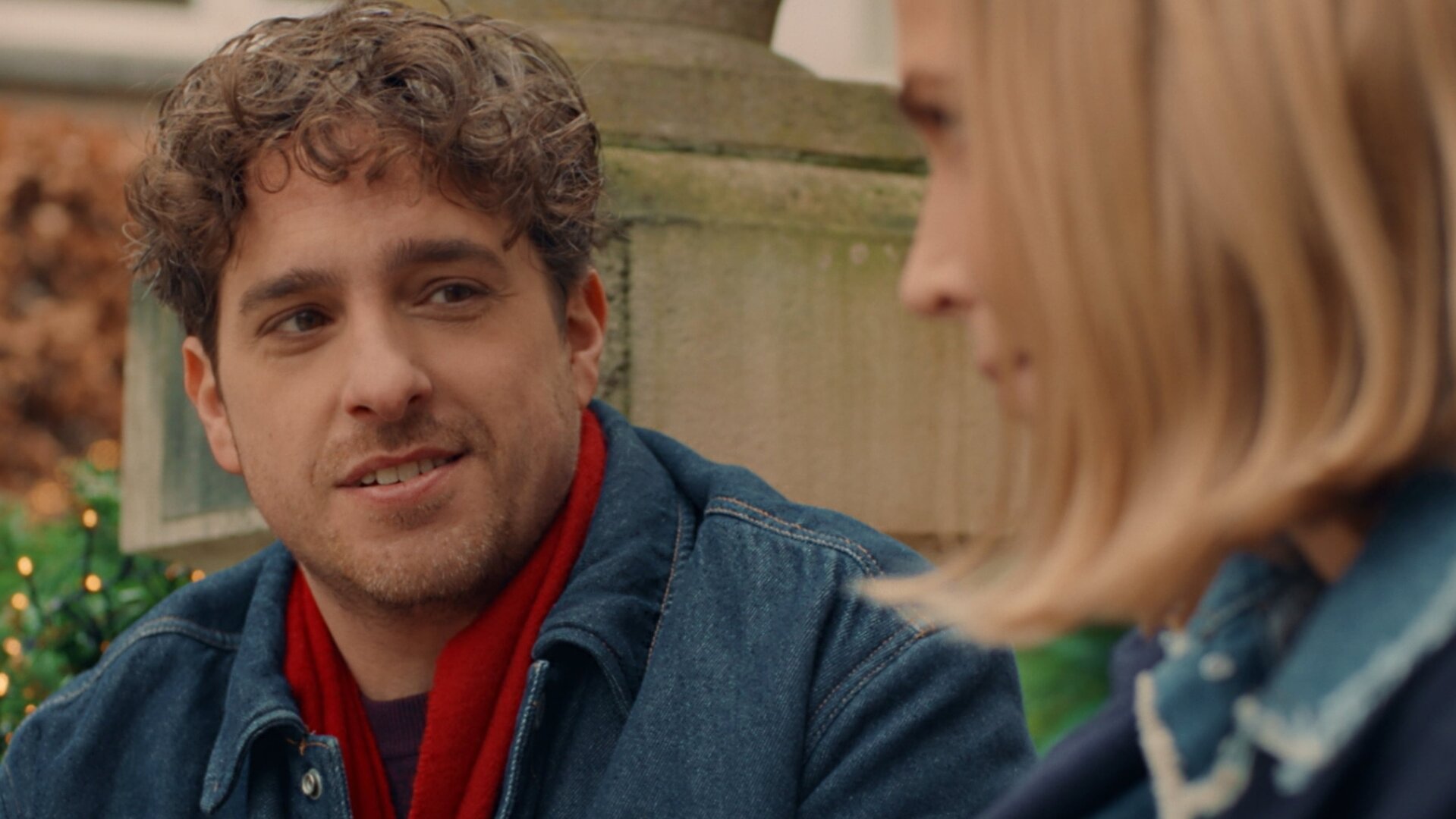 "Single Bells - 12 Dates till Christmas: Fonny": Fonny (Jelle De Beule) wirft Mina (Julie Van den Steen) einen flirtenden Blick zu. Er hat gelocktes Haar und trägt einen Dreitagebart.