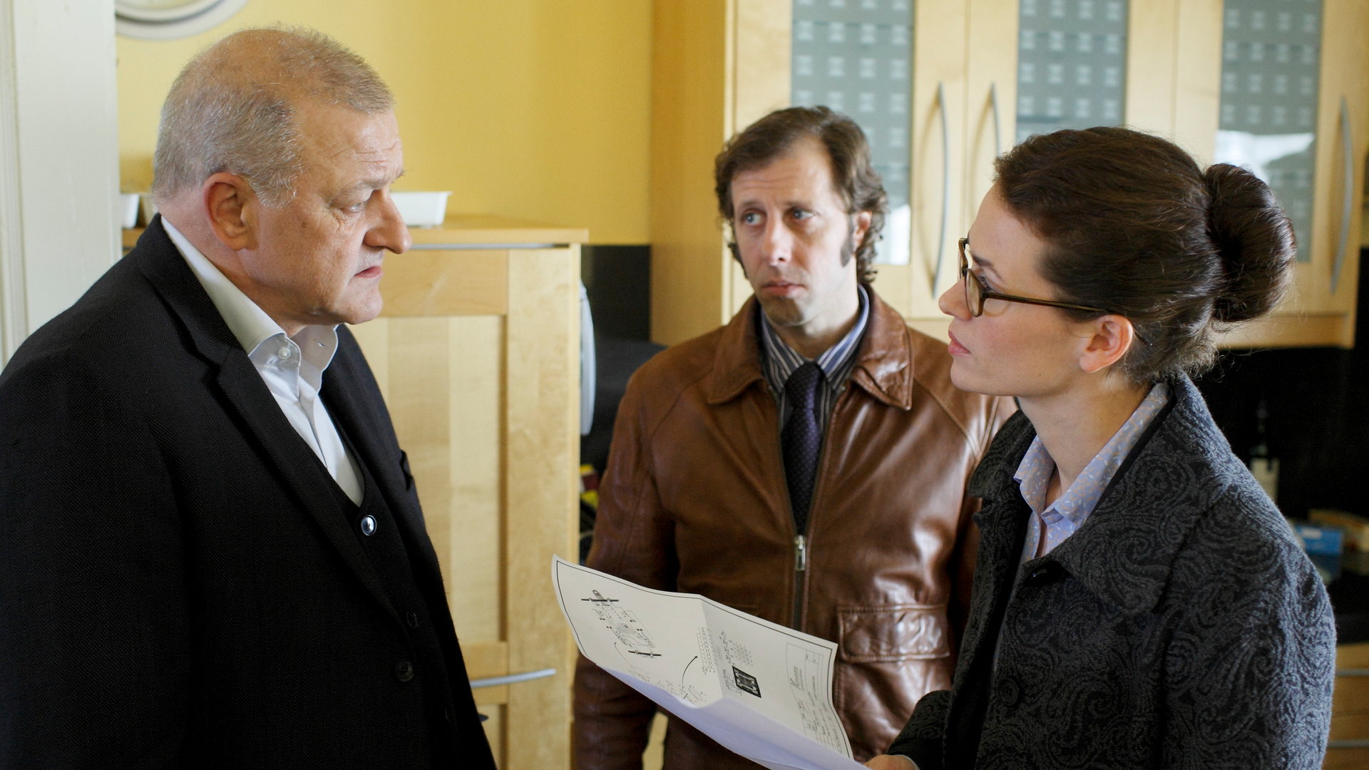 "Wilsberg - Gefahr im Verzug": Wilsberg (Leonard Lansink) spricht mit Karla Berhenke (Melika Foroutan), die Unterlagen in der Hand hält. Ekki Talkötter (Oliver Korittke) steht etwas irritiert daneben.