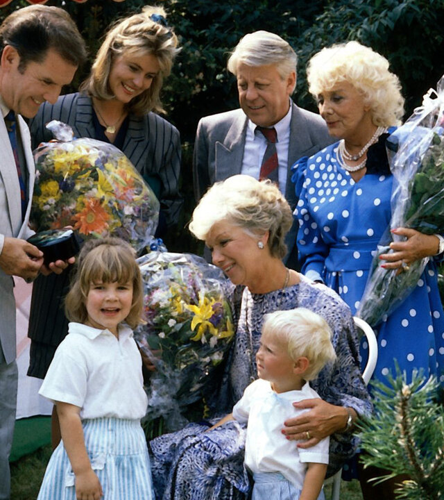 "Die Wicherts von nebenan: Hannelore wird 50": In einem Garten. Hannelore (Maria Sebaldt) hat Geburtstag und steht im Kreise ihrer Familie. Sie schaut liebevoll auf ihre beiden Enkelkinder. Drei der Gratulanten haben Blumensträuße in der Hand.