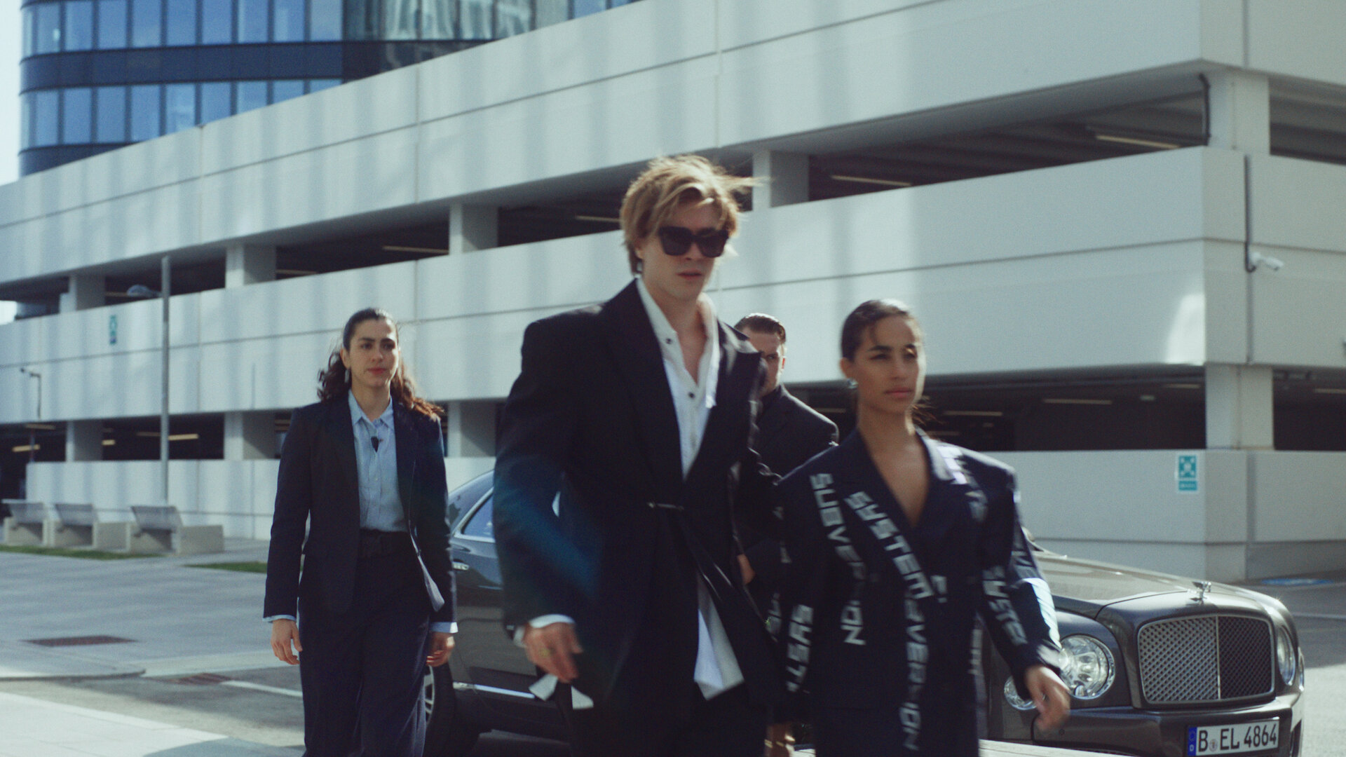 "Crystal Wall - Vertrauen": Louna Lloris (Anna Bardavelidze) begleitet Nicolas Dardenne (Gustav Schmidt) und Dita (Gizem Emre) zu einem Geschäftstermin. Sie laufen mit ernsten Blick auf einer Straße vor einem geparkten Auto.
