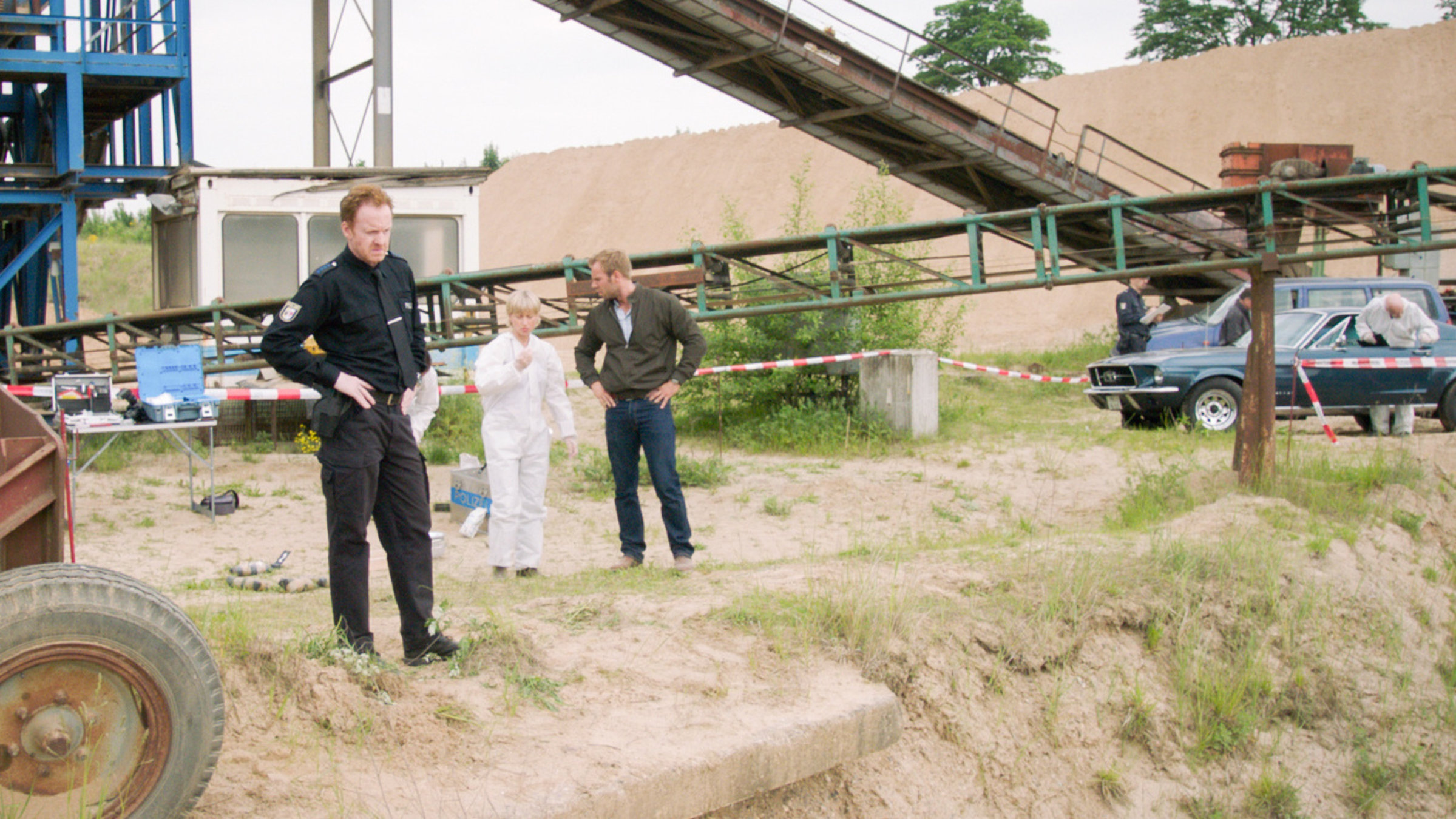 "SOKO Wismar – Schnee aus Kolumbien": Timmermann (Mathias Junge) schaut von oben hinab in eine Kiesgrube, wo das Opfer gefunden wurde. Roswitha Prinzler (Silke Matthias) und Lars Pöhlmann (Dominic Boeer) unterhalten sich im Hintergrund über die ersten Ergebnisse der Spurensicherung.