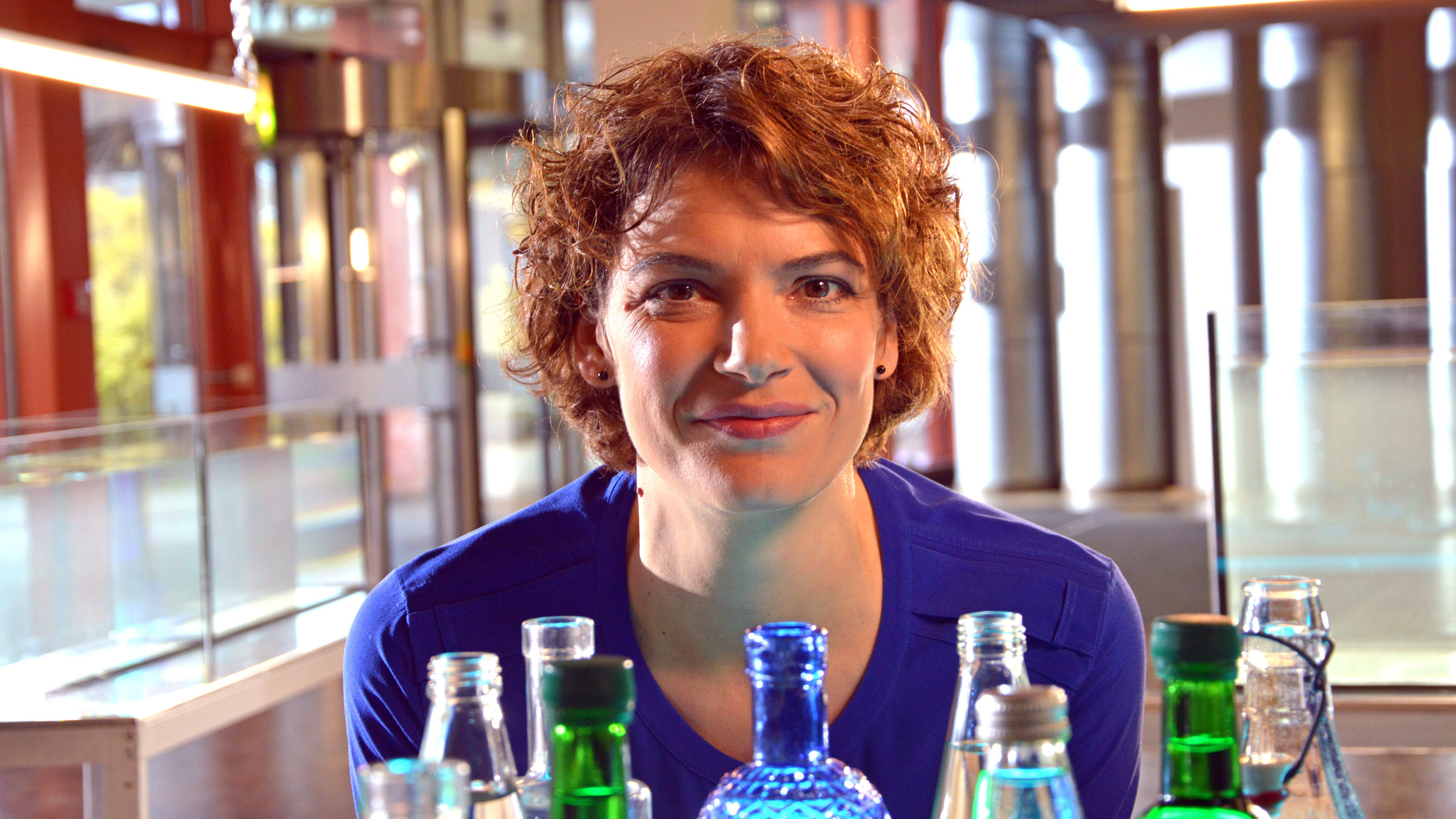 "Terra Xpress: Zeit für gutes Wasser": Moderatorin Lena Ganschow in Großaufnahme hinter verschiedenen Flaschen.
