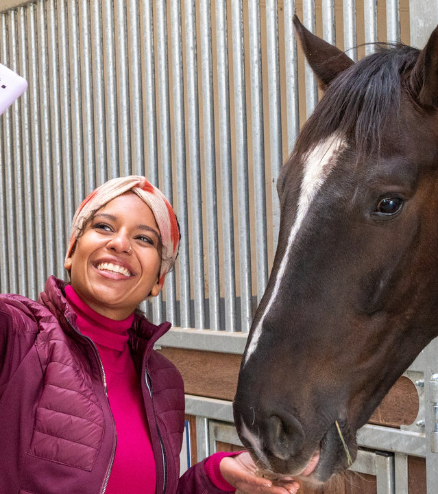 "SOKO Stuttgart – Alles Glück dieser Erde": Reitinfluencerin Nina Franke (Souhaila Amade) steht in einem Pferdestall und strahlt in die Kamera ihres Handys. Sie macht von sich und einem Pferd, das den Kopf aus einer Stallbox streckt, ein Selfie. Sie hält dem Pferd eine Belohnung hin, welches dies aus ihrer flachen Hand futtert.