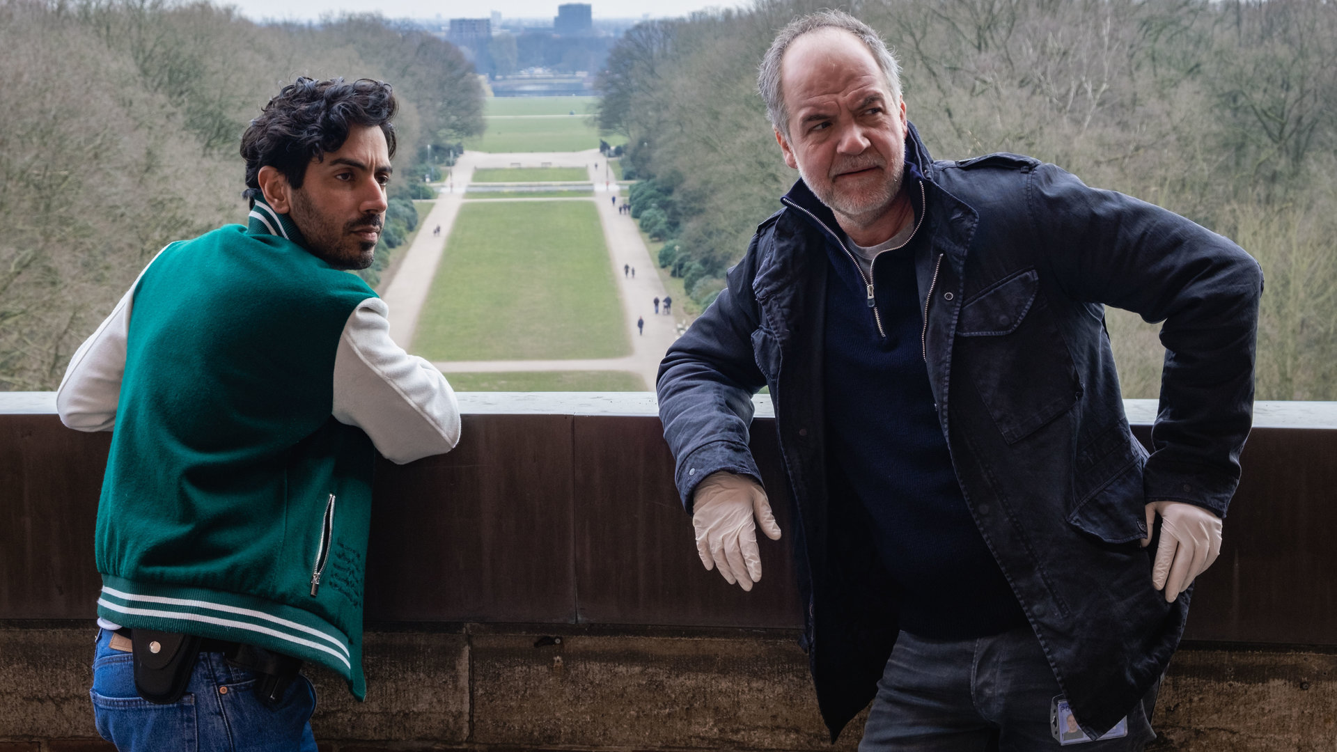 "SOKO Hamburg - Das Fenster zum All": Luiz Vieira dos Santos (Thiago Braga de Oliveira) und Oskar Schütz (Marek Erhardt) stehen auf einer Aussichtsplattform und blicken nachdenklich nach rechts. Luiz hat sich mit den Armen auf die Brüstung der Plattform gestützt. Oskar Schütz lehnt mit dem Rücken an der Brüstung und trägt weiße Gummihandschuhe.