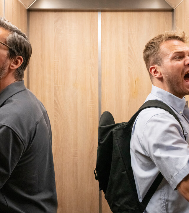 "Like a Loser: Wie soll man da ernst bleiben": Guideon (Tom Beck, l.) und Julian Beil (Ben Münchow, r.) befinden sich in einem kleinen, steckengebliebenen Aufzug. Guideon hämmert mit der Faust verzweifelt gegen die hölzerne Wand des Aufzugs und ruft nach Hilfe. Julian klatscht mit der flachen Hand gegen die gegenüberliegende Wand und schreit ebenfalls lautstark. Beide wirken aufgebracht und genervt.