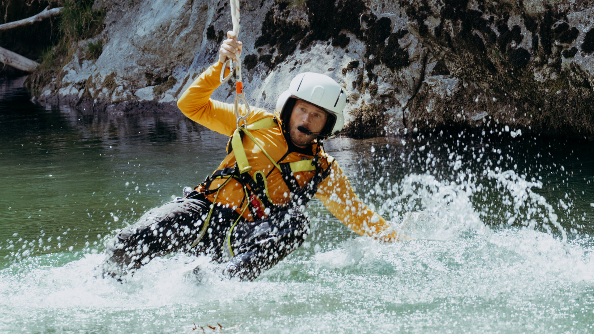 "Die Bergretter: Ohne Ausweg": In einem Wildbach: Bergretter Markus Kofler (Sebastian Ströbel) hängt am Rettungstau. Seine Beine sowie der linke Arm sind ins aufwirbelnde Wasser getaucht. Er blickt konzentriert.