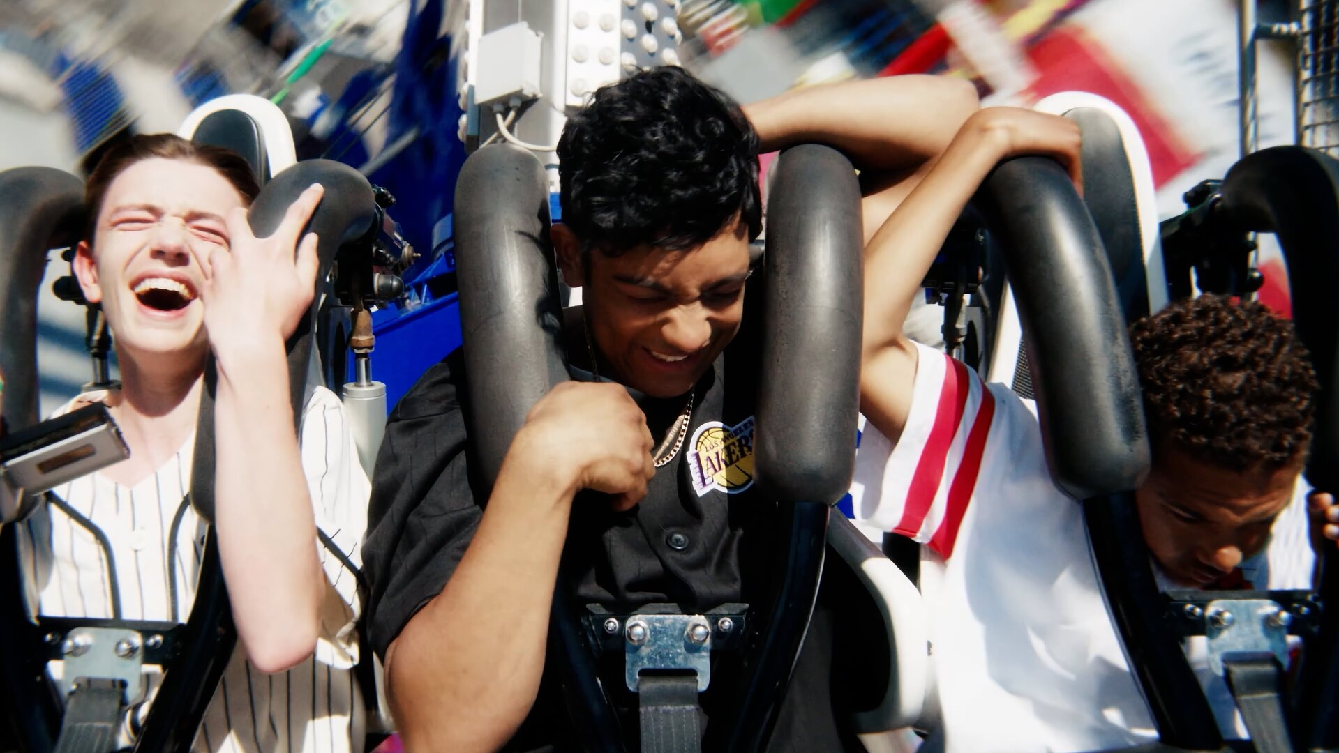 "After Benjamin: Neverland": Espen (Magnus Johan Tenfjord), Omer (Benjamin Ahmed) und Jama G (Nickolai Sødal Kabanda) sitzen nebeneinander in einer fahrenden Achterbahn. Sie halten sich an den Sicherheitsbügeln fest und haben sichtlich Spaß.