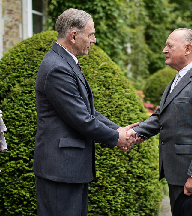 "An einem Tag im September": Charles de Gaulle (Jean-Yves Berteloot) und Konrad Adenauer (Burghart Klaußner) stehen sich vor dem Landhaus gegenüber und begrüßen sich mit einem Handschlag. Hinter de Gaulle stehen seine Frau Yvonne (Hélène Alexandridis) und sein Sohn Philippe (Pierre Lognay) und beobachten das Ganze. Günther Bachmann (Fabian Busch) steht etwas abseits hinter Adenauer und sieht ebenfalls zu.