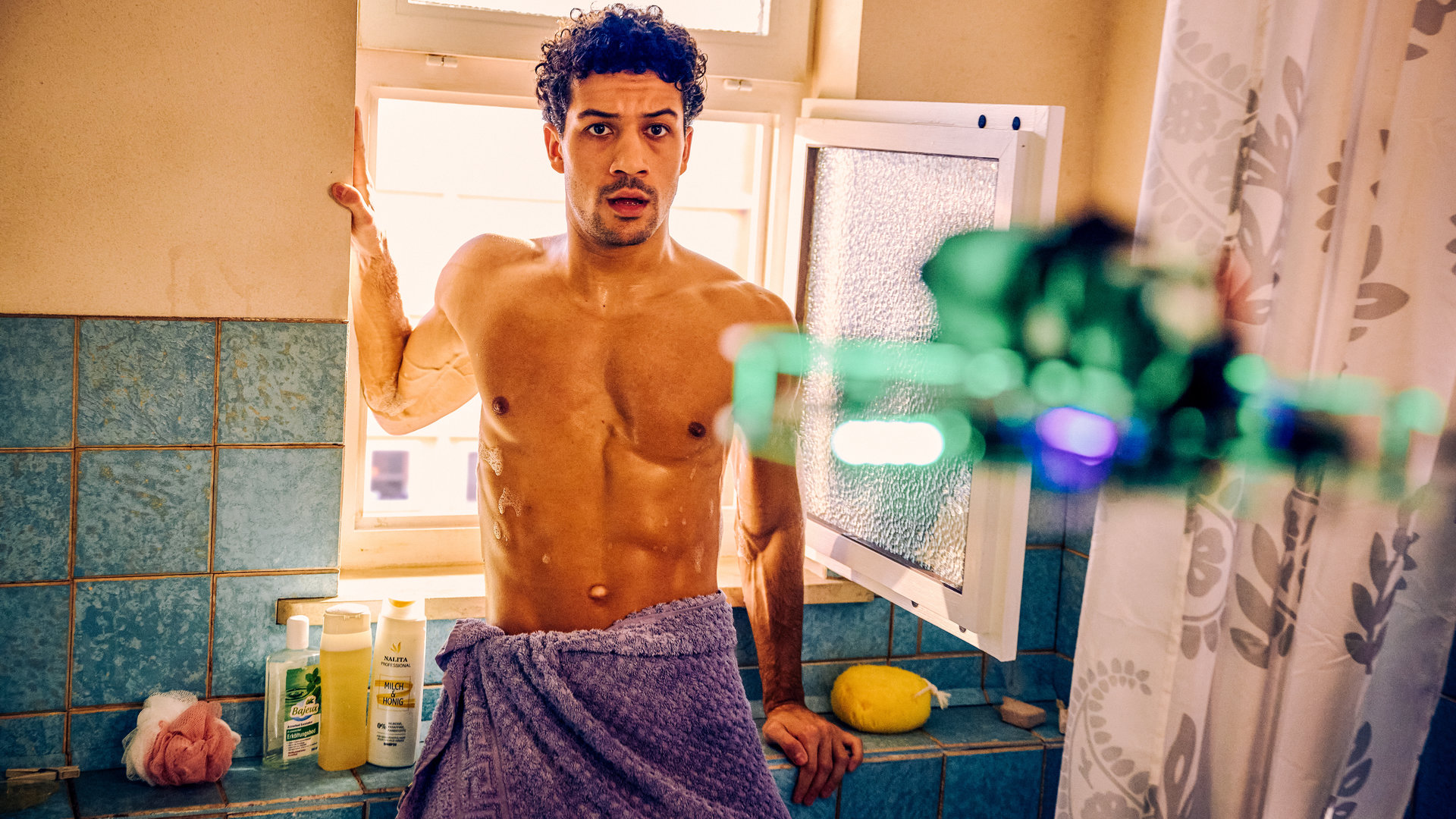 "Ich dich auch! - Der Dosenöffner": Yannik (Rojan Juan Barani) steht mit nacktem Oberkörper im Badezimmer und starrt auf eine Drohne die direkt auf ihn zukommt.