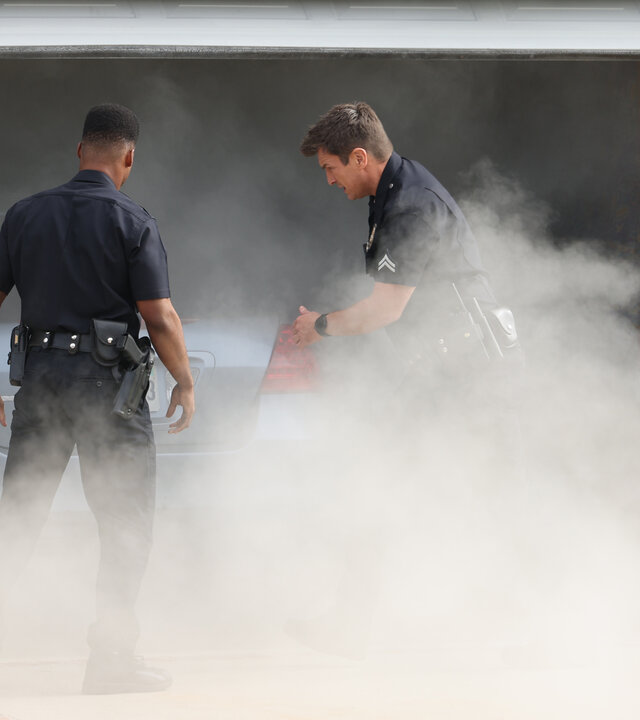 "The Rookie - Neue Wege": Officer Nolan (Nathan Fillion) und Officer Aaron Thorsen (Tru Valentino) stehen vor einer Garage, aus der dichte Schwaden von Rauch hervorquellen.