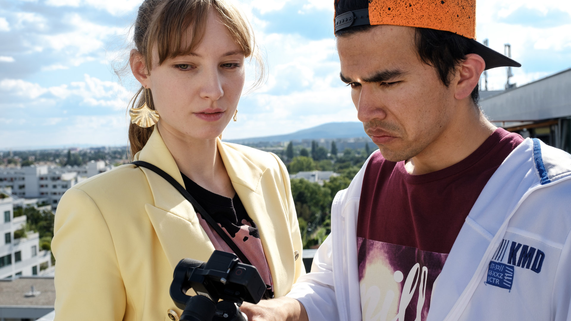 "SOKO Wien - Nahaufnahme": Auf einem Balkon stehen Dani (Julia Roy) und Flo (Bagher Ahmadi). In einer Hand hält Flo Neubauer eine Kamera, auf die beide Protagonisten schauen.