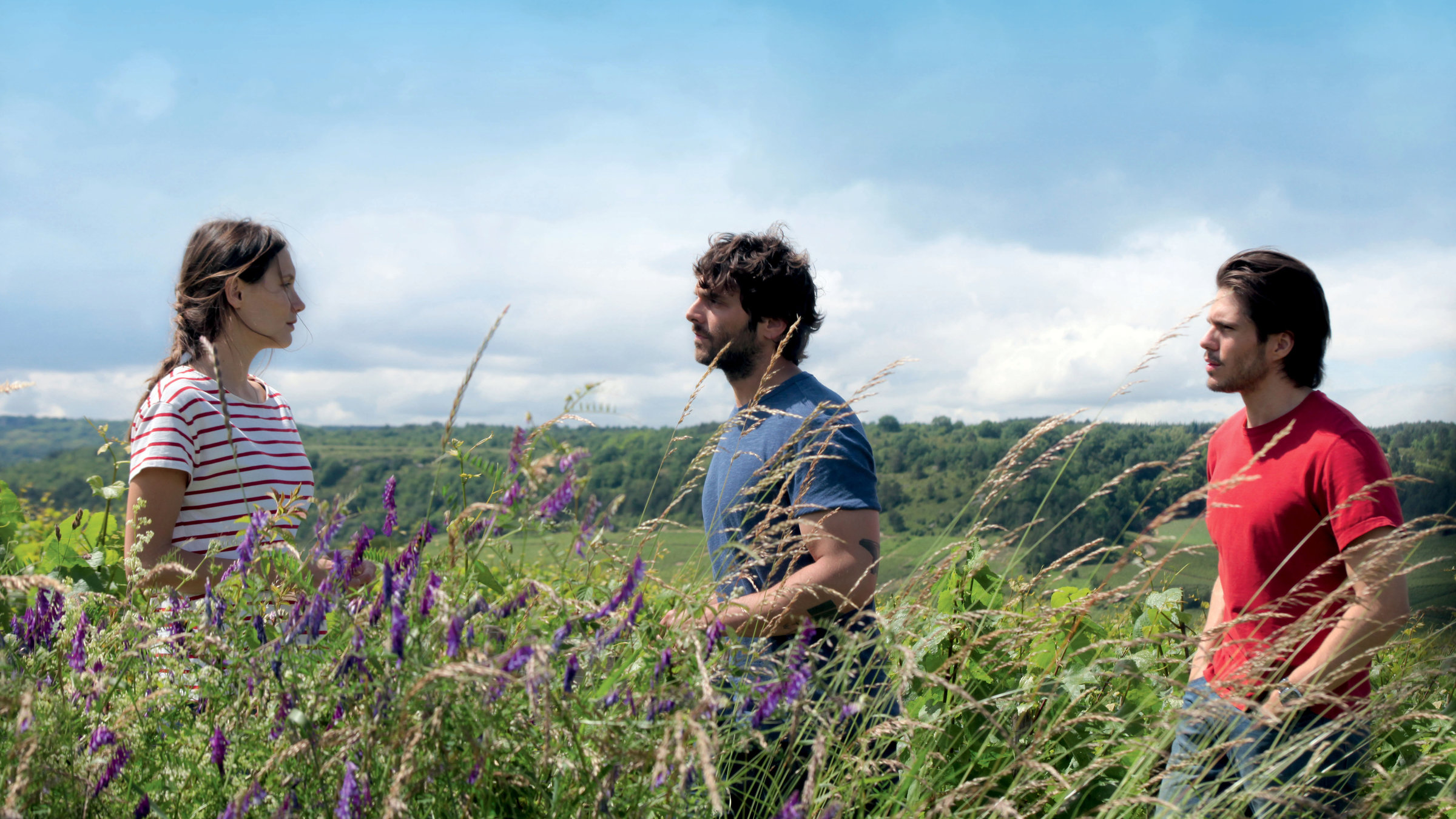 "Der Wein und der Wind": Die Geschwister Jean (Pio Marmaï), Juliette (Ana Girardot) und Jérémie (François Civil) stehen an ihrem Weinberg, zwischen blühenden Feldblumen.