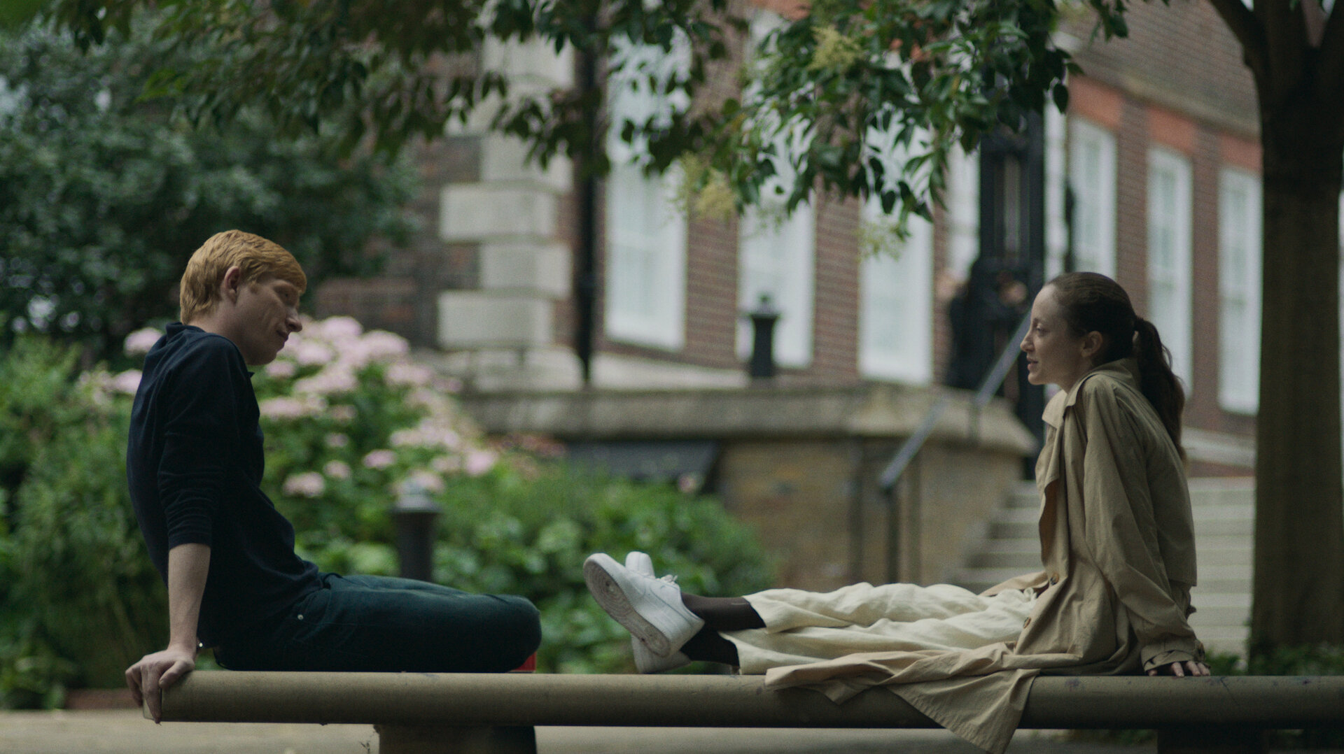 "Alice & Jack - Zu zweit": Jack (Domhnall Gleeson) sitzt auf einer Steinbank in einem Park. Ihm gegenüber sitzt Alice (Andrea Riseborough). Sie hat die Beine auf die Bank gelegt und schaut ihn an. Beide wirken ins Gespräch vertieft.