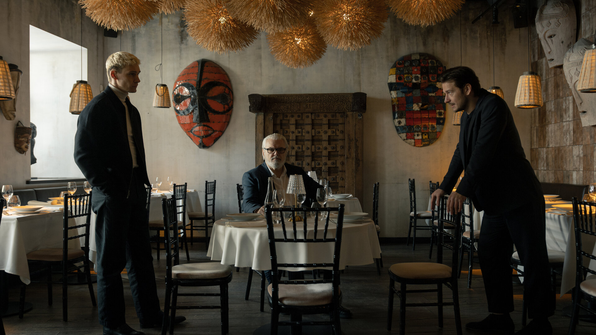 "Serial Cleaner - Absolute Stille": Ludwig Karanz (László I. Kish) sitzt am Tisch im Restaurant. Seine beiden Söhne Christian Karanz (Rick Okon) und Vincent Karanz (Stefan Gorski) stehen sich davor angespannt gegenüber.