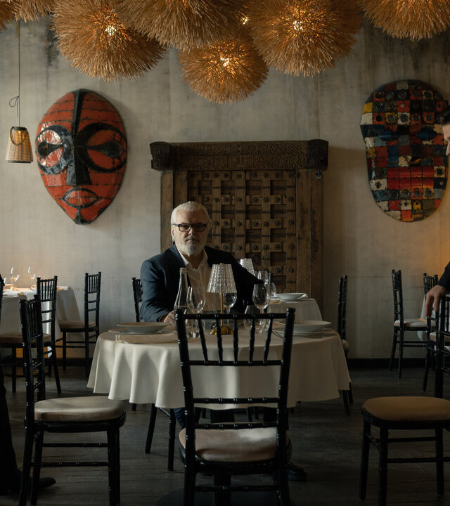 "Serial Cleaner - Absolute Stille": Ludwig Karanz (László I. Kish) sitzt am Tisch im Restaurant. Seine beiden Söhne Christian Karanz (Rick Okon) und Vincent Karanz (Stefan Gorski) stehen sich davor angespannt gegenüber.