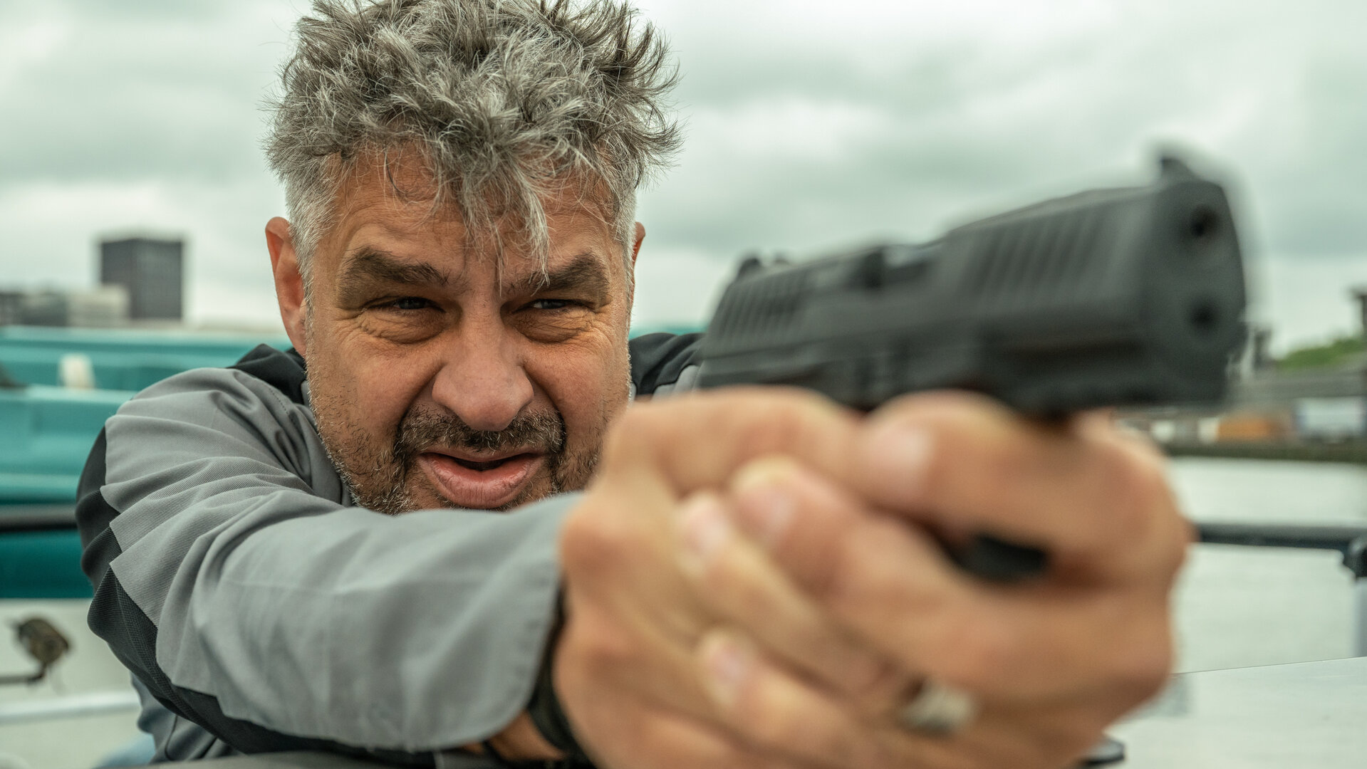 "Blind Sherlock - Pfannkuchenschiff": Nico (Frank Lammers) steht auf einem Boot. Er hält seine Pistole mit beiden Händen und visiert ein Ziel an.