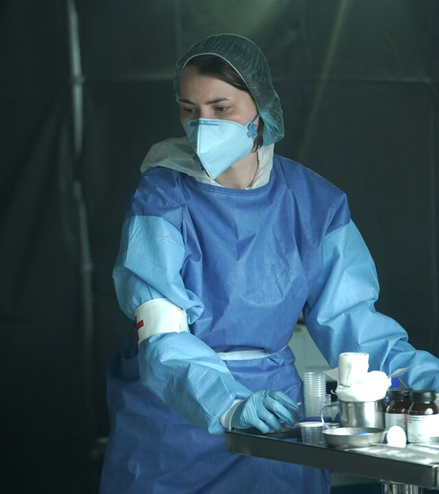 "Sløborn III – Klabaster sterben einsam": Yvonne (Linda Stockfleth) steht in voller Schutzkleidung im Krankenhauszelt vor einem kleinen Metalltisch mit Medikamenten und Verbandszeug.