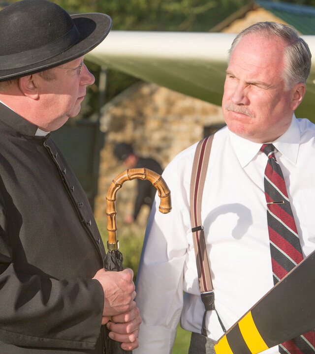 "Father Brown - Der vermisste Mann": Father Brown (Mark Williams) steht mit Arthur Le Broc (Rupert Vansittart) auf dem Flugplatz. Sie unterhalten sich. Neben Arthur steht eine Propellermaschine.