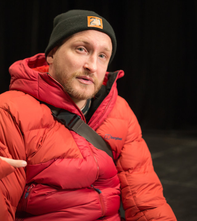 "einfach Mensch: Graf Fidi: Ich mach das mit links": Graf Fidi mit roter Daunenjacke und einer dunklen Mütze auf einer Bühne.