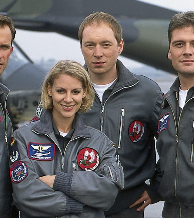 "Die Rettungsflieger - Rivalen im Cockpit": Teamaufnahme von Jens Blank (Nicolas König), Sabine Petersen (Marlene Marlow), Paul Reinders (Rainer Sellien) und Jan Wollcke (Oliver Hörner) auf dem Flugplatz. Im Hintergrund ein Transportflugzeug und ein Hubschrauber.