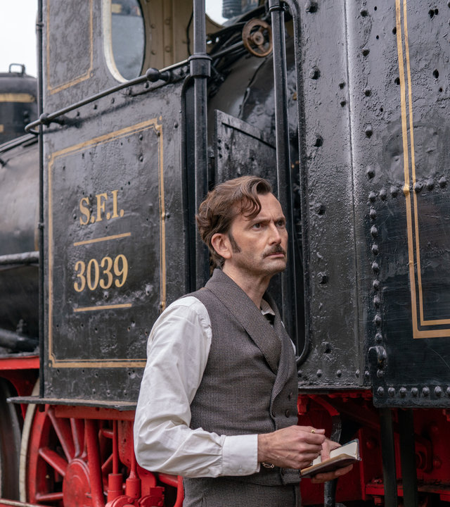 "In 80 Tagen um die Welt (2)": Phileas Fogg (David Tennant) steht seitlich vor einer Dampflokomotive und hält ein Notizbuch in seiner Hand.