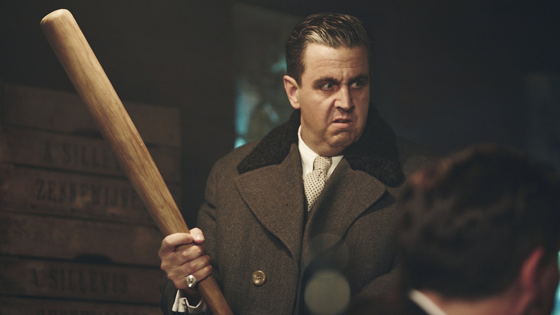 "Sketch History": Al Capone (Bastian Pastewka) steht mit Gangsterfrisur und schickem Mantel in einem schummrig beleuchteten Raum und hält mit beiden Händen einen Baseballschläger. Er blickt bedrohlich.