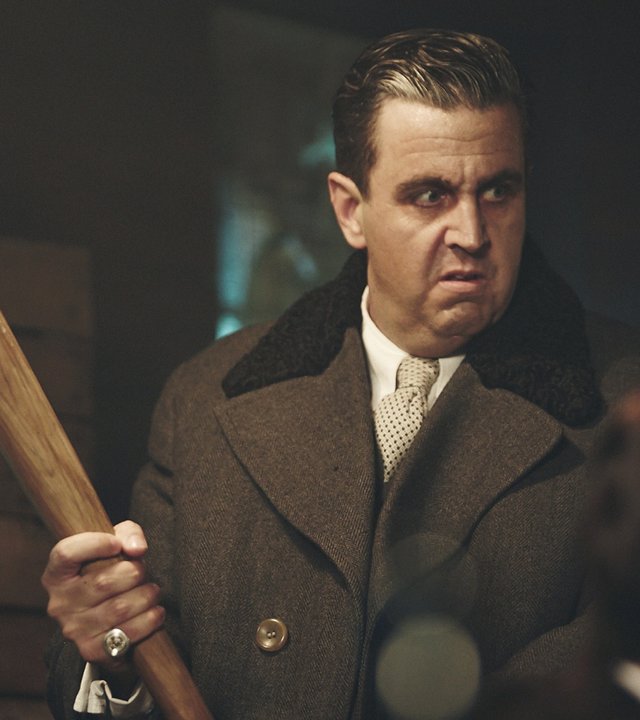 "Sketch History": Al Capone (Bastian Pastewka) steht mit Gangsterfrisur und schickem Mantel in einem schummrig beleuchteten Raum und hält mit beiden Händen einen Baseballschläger. Er blickt bedrohlich.