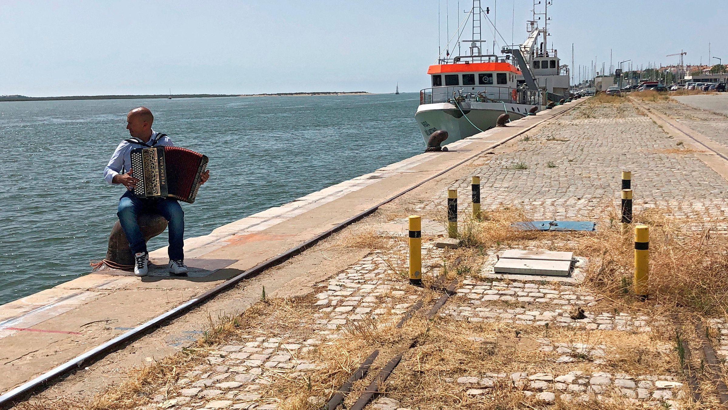 "An der Sandalgarve in Portugal - Blaue Züge, blaues Meer": An der Mole in Vila Real de Santo António filmen wir einen Musiker, der das Akkordeon, das traditionelle Instrument der Algarve beherrscht.
