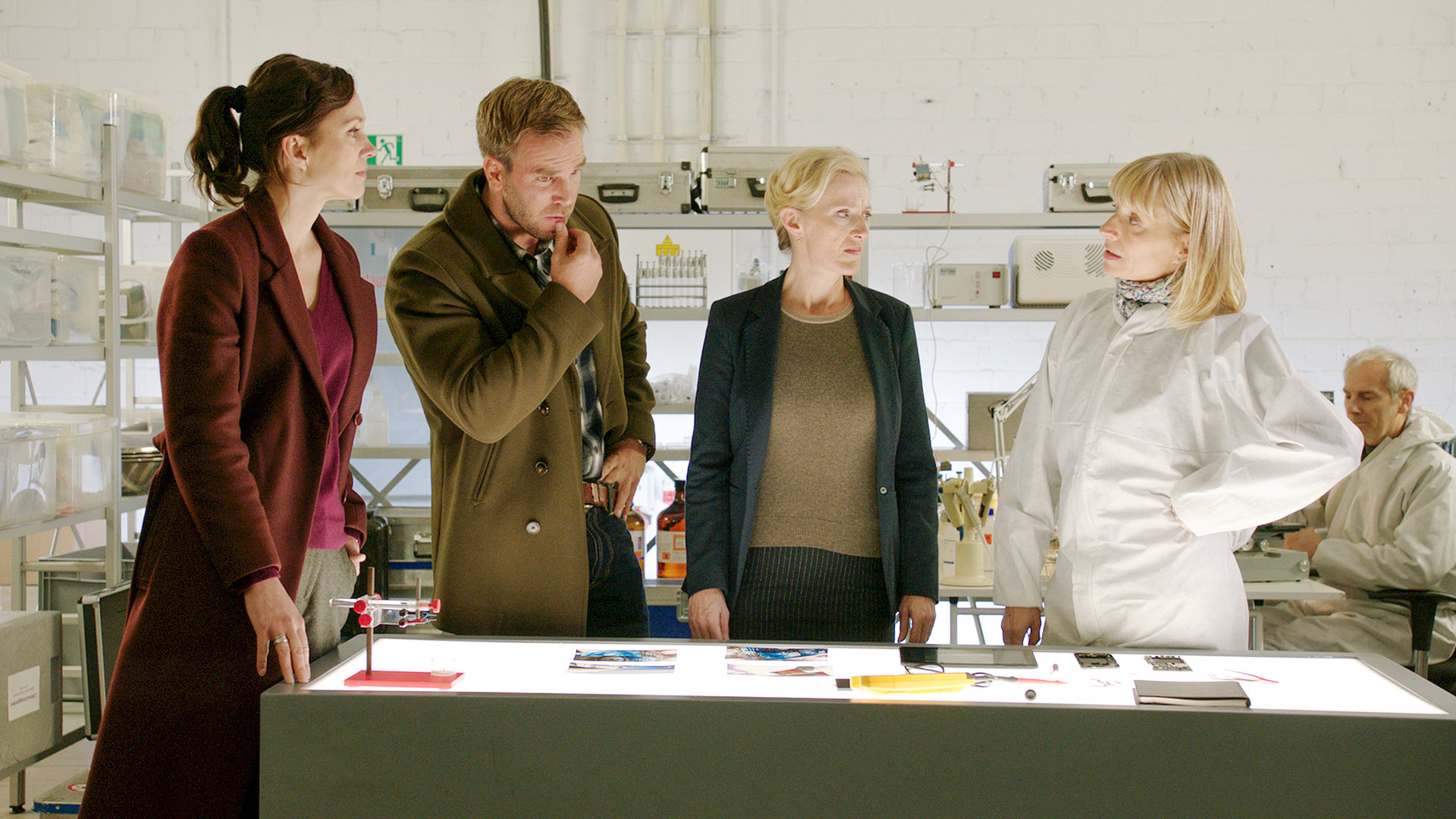 „SOKO Wismar: Yacht-Jäger“: Im Labor der Kriminaltechnik stehen Karoline Joost (Nike Fuhrmann), Lars Pöhlmann (Dominic Boeer) Roswitha Prinzler (Silke Matthias) und Anna Heep (Katharina Hoffmann) um einen Tisch herum. Roswitha und Karoline sehen zu Anna, während Lars sich nachdenklich ans Kinn fasst und auf den Tisch vor ihnen blickt.