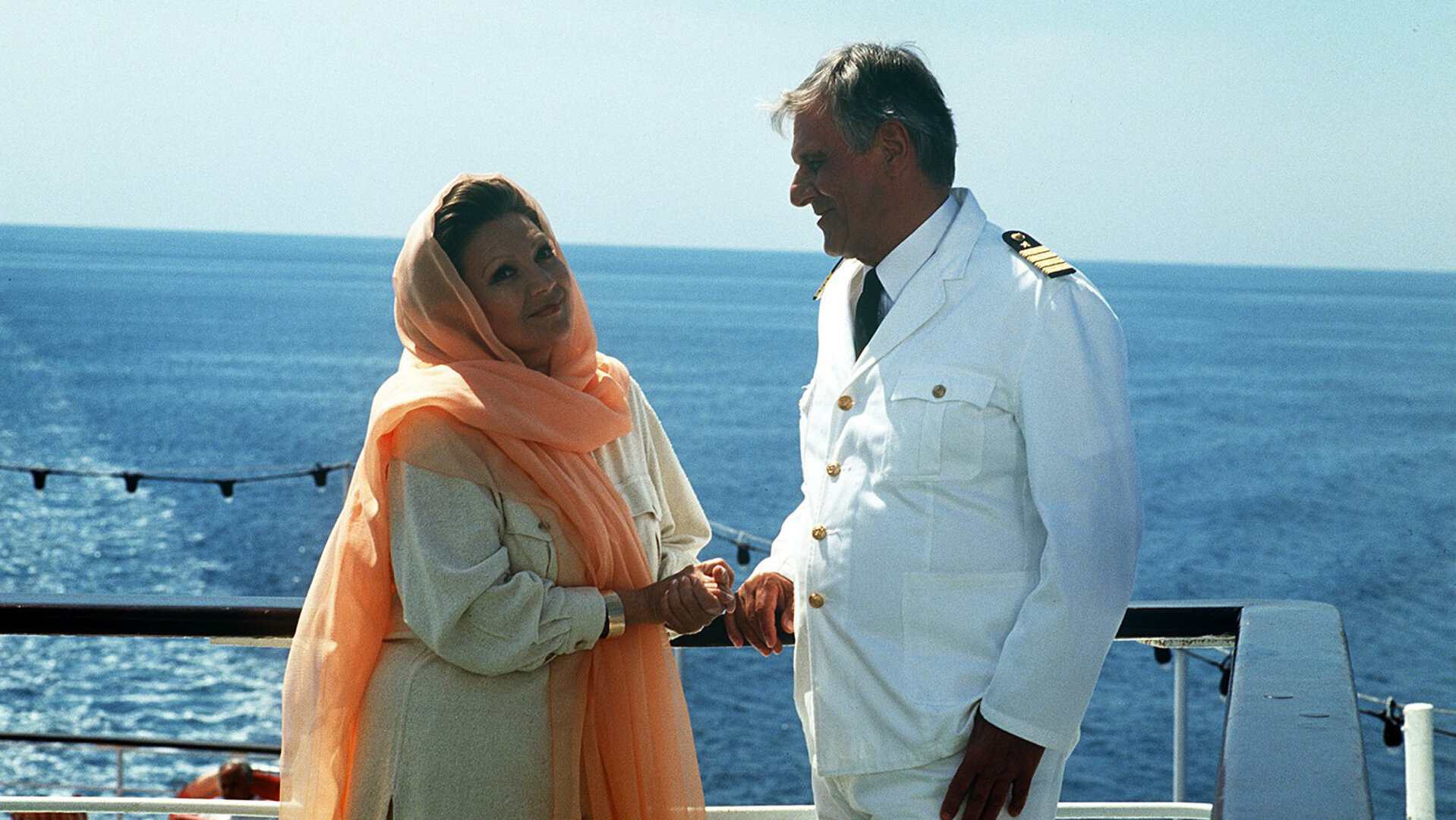 "Das Traumschiff - Florida": Madame Sarat Sakarian (Louise Martini) steht neben Kapitän Heinz Hansen (Heinz Weiss) an der Reling eines Schiffes und blickt verschwörerisch in die Kamera.