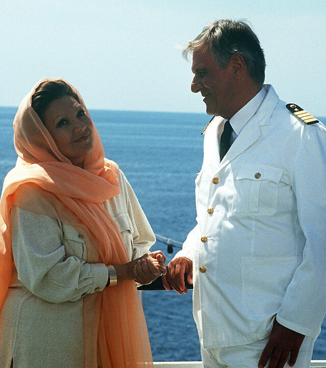 "Das Traumschiff - Florida": Madame Sarat Sakarian (Louise Martini) steht neben Kapitän Heinz Hansen (Heinz Weiss) an der Reling eines Schiffes und blickt verschwörerisch in die Kamera.