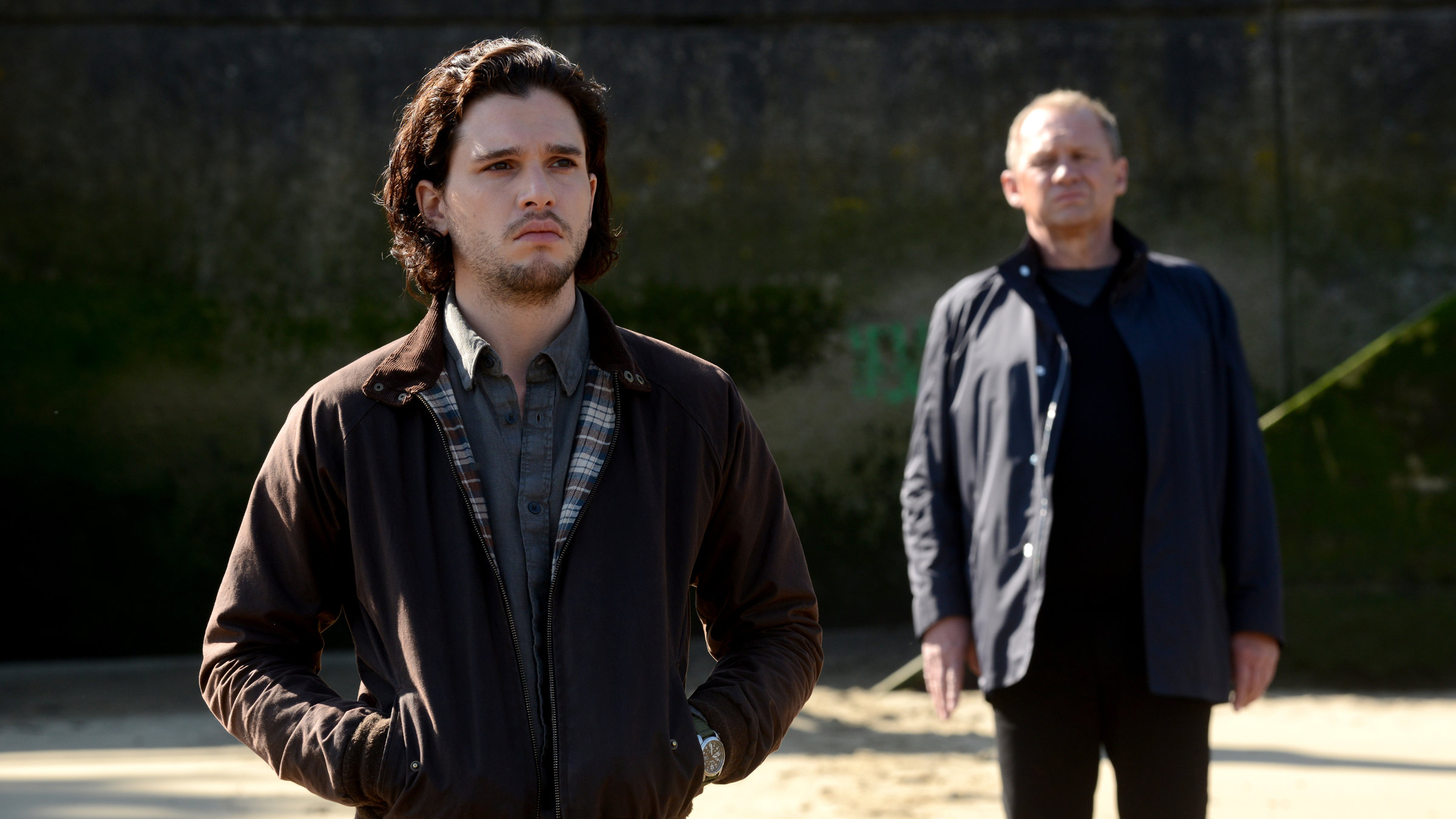 "Spooks - Verräter in den eigenen Reihen": Harry (Peter Firth) und Will (Kit Harington)  stehen hintereinander am Strand, beide blicken nach vorne. Will hat die Hände in der Jackentasche. Sein trauriger Blick verliert sich im Unbestimmten, während Harry abwartet.