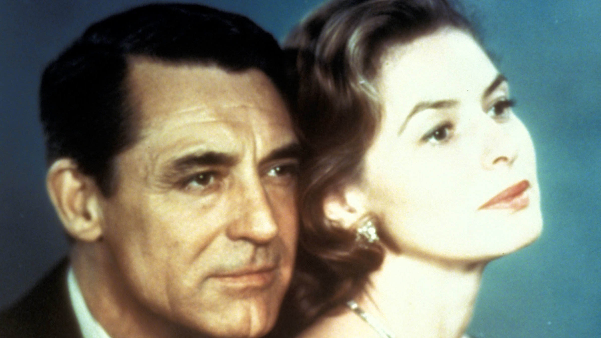 "Indiskret": Philip Adams (Cary Grant) steht ganz nah hinter Anna Kalman (Ingrid Bergman) und hat seine rechte Hand auf ihren rechten Oberarm gelegt. Beide tragen elegante Abendgarderobe. Ihr beider Blick richtet sich auf einen Punkt außerhalb des Bildausschnitts.