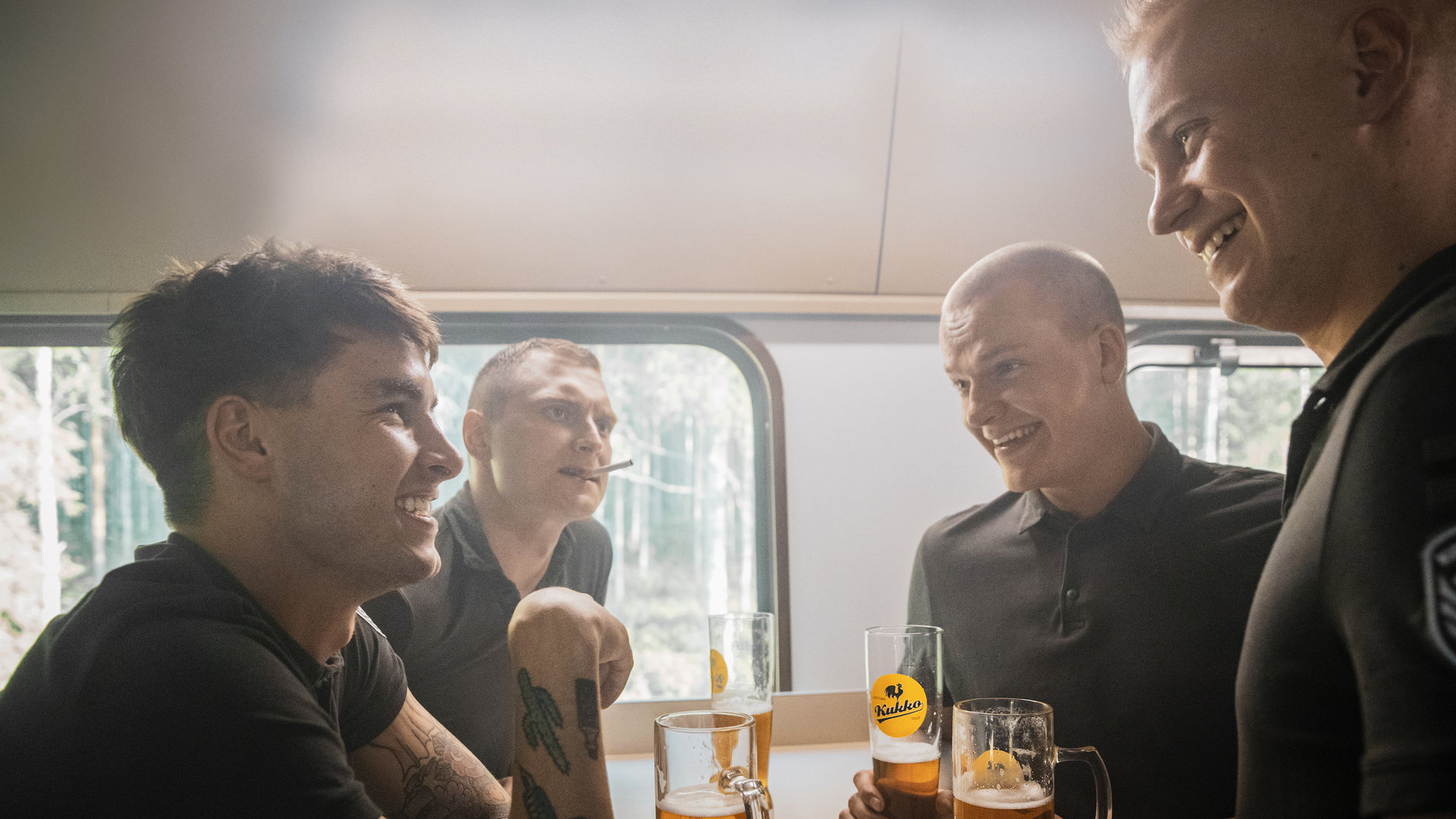 "Californian Commando - Der Besuch": Van (Kian Lawley) und seine Kameraden Soukka (Elias Keranen), PH (Juho Uusitalo) und Forsbacka (Tatu Sinisalo) sitzen sich an einem Tisch im Zug gegenüber und trinken Bier.