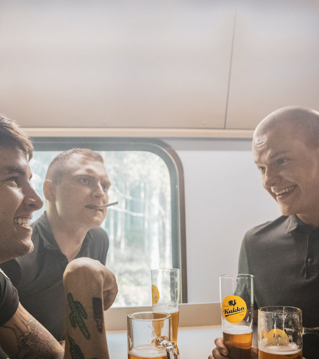 "Californian Commando - Der Besuch": Van (Kian Lawley) und seine Kameraden Soukka (Elias Keranen), PH (Juho Uusitalo) und Forsbacka (Tatu Sinisalo) sitzen sich an einem Tisch im Zug gegenüber und trinken Bier.