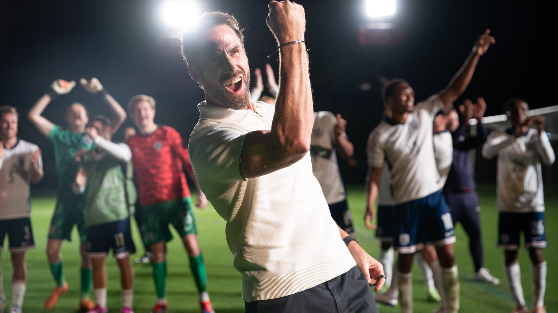 "Dear England (4)": Bei Flutlicht nachts im Stadion auf dem Rasen: Im Vordergrund reckt Gareth Southgate (Joseph Fiennes) seinen rechten Arm mit geballter Faust vor Kraft strotzend in die Höhe. Hinter ihm befindet sich seine Mannschaft, die ebenfalls jubiliert.