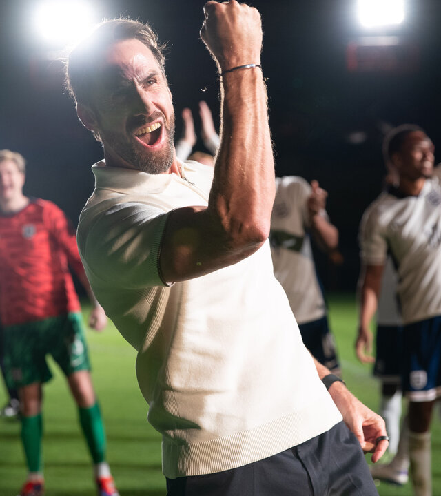 "Dear England (4)": Bei Flutlicht nachts im Stadion auf dem Rasen: Im Vordergrund reckt Gareth Southgate (Joseph Fiennes) seinen rechten Arm mit geballter Faust vor Kraft strotzend in die Höhe. Hinter ihm befindet sich seine Mannschaft, die ebenfalls jubiliert.