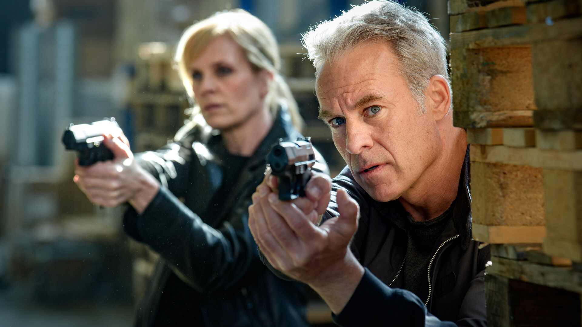 "SOKO Leipzig - Was bleibt (1)": Ina Zimmermann (Melanie Marschke) und Jan Maybach (Marco Girnth) stehen mit gezogenen Waffen hinter einem Stapel Paletten.