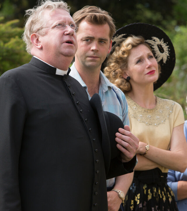 "Father Brown - Die Moral des Henkers": Father Brown (Mark Williams), Sid Carter (Alex Price), Lady Felicia (Nancy Carroll) und Mrs. McCarthy (Sorcha Cusack) stehen nebeneinander im Garten und schauen in eine Richtung.