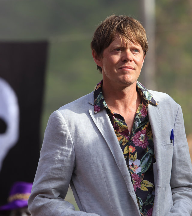 "Death in Paradise: Der Mann, den es nicht gab": Humphrey (Kris Marshall) steht im Freien vor einer schwarzen Flagge auf der ein weißer Totenkopf zu sehen ist.