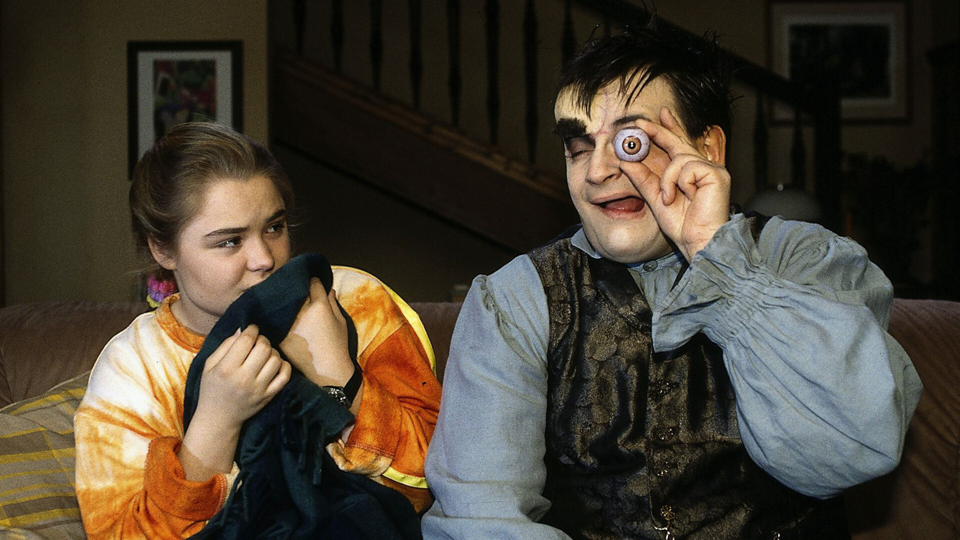 "Sprechstunde bei Dr. Frankenstein": Lenni (Michael Trischan) und Franzi (Fritzi Eichhorn) sitzen nebeneinander auf dem Sofa. Lenni hält sich ein künstliches Auge vor sein Auge.