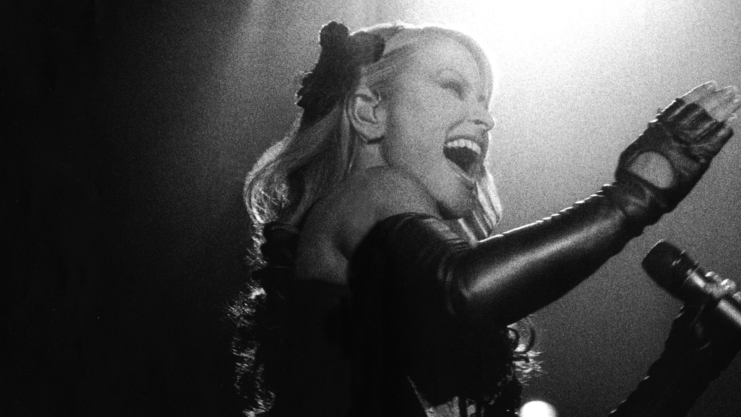 "Anastacia: Live at Last": (s/w) Seitlicher Blick auf die Sängerin Anastacia. Sie steht vor einem Mikrofon und singt. Ein Arm ist angewinkelt und zeigt in die Höhe. Die Sängerin trägt Lederstulpen.