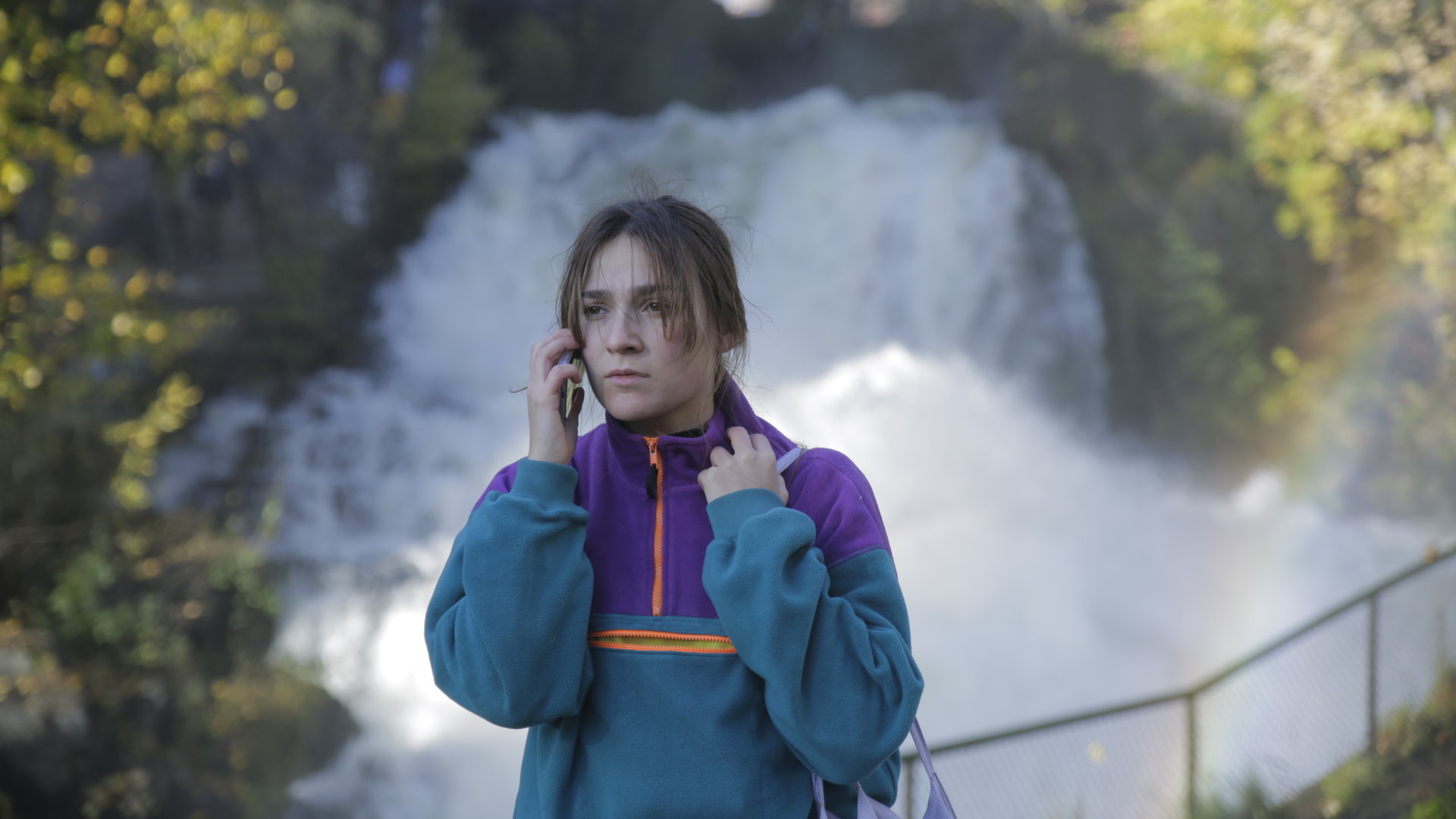 "About Saturday - Suck it up": Klara (Darin Hagi) steht vor einem Wasserfall und telefoniert mit ihrem Handy.
