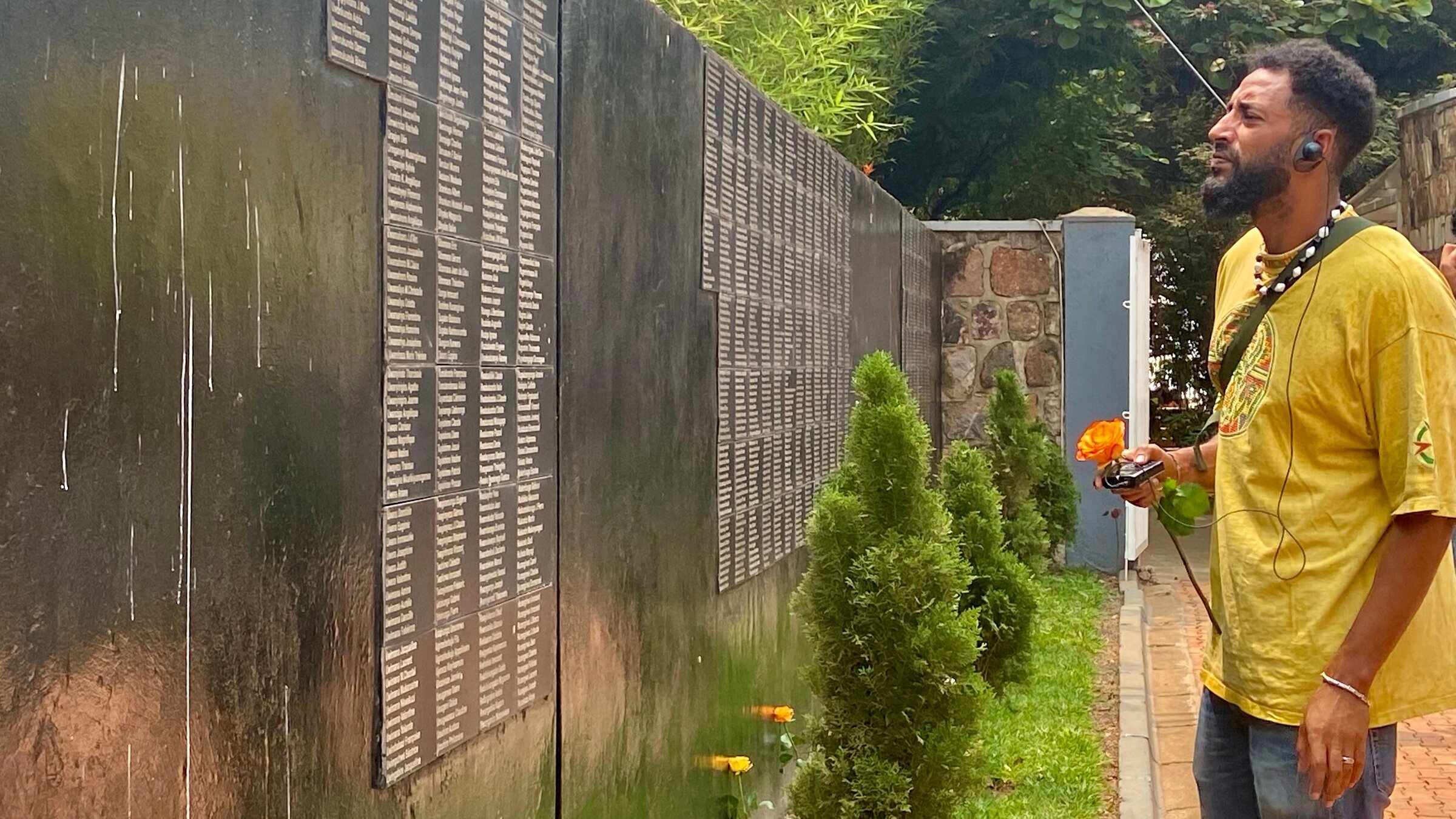 "37°: Ererbtes Trauma - Julien und der Schmerz der Anderen": Julien (35) steht im "Genocide Memorial Center" in Kigali vor einer Gedenktafel mit vielen Namen von ermordeten Tutsi. Er hält eine Rose in der Hand.