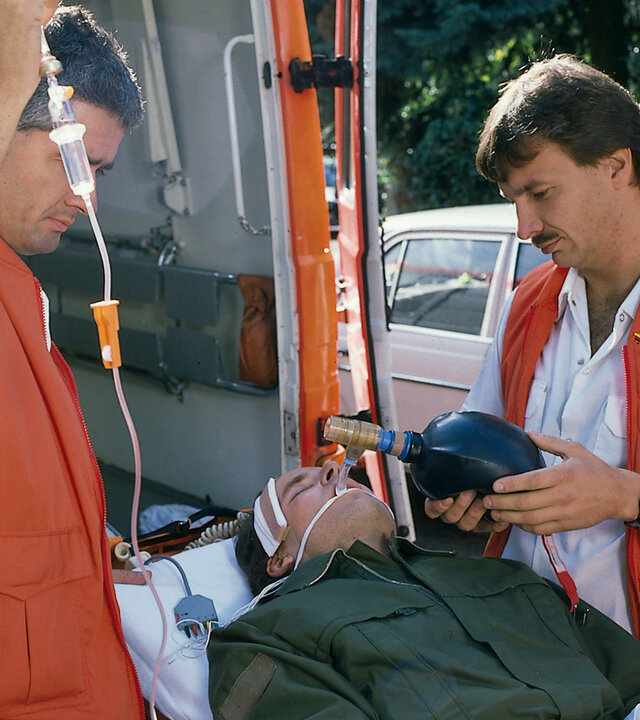 "Diese Drombuschs - Der Makel": Chris (Mick Werup) liegt mit einem Kopfverband auf einer Trage und wird in den Krankenwagen geschoben. Links und rechts und von ihm stehen Sanitäter.