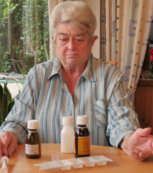 "37° Bloß nicht krank werden - Menschen ohne Krankenversicherung": Helga S. sitzt an einem Tisch im Wohnzimmer. Vor ihr stehen Medikamente und sie schaut drauf.